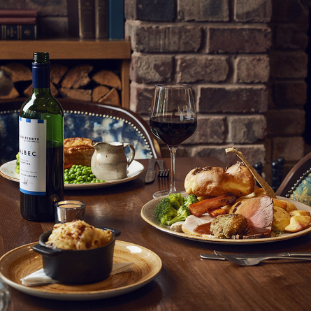 A roast dinner on a table next to a glass of red wine.