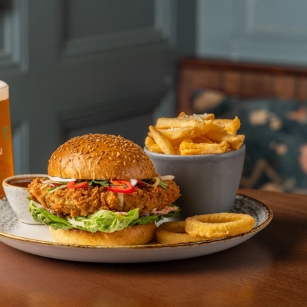 A burger served on a plate with chips, onion rings and sauce, sitting on a table next to a glass of Level Head ale.