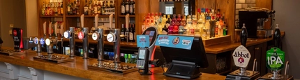 A close up view of the bar at The Vine Inn in Ower, with bottles of wine and alcoholic spirits on wooden shelves behind the counter.