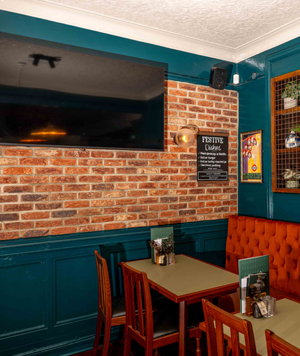 An interior restaurant seating area of the Lucas Arms in London, with upholstered booth seating and a TV on the wall.
