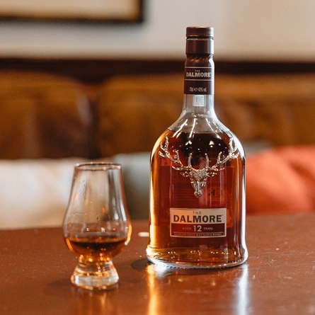A bottle of The Dalmore Whisky on a table next to a whisky glass.