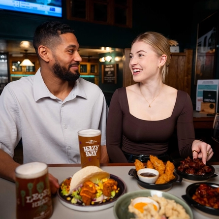 An image focusing on 2 people within a group of friends sat at a table within the restaurant area with a small plates dishes and drinks available at Urban Social venues.