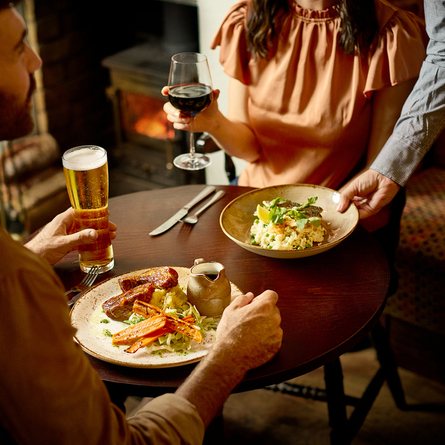 An image of 2 customers being served food with various drinks within the interior restaurant seating area at a Chef & Brewer venue.