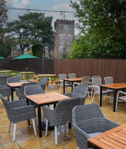 The paved exterior beer garden seating area at the Tredegar Arms, with shade umbrellas on two of the tables, and string lights overhead.
