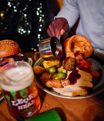 A image of gravy being poured over a roast meal within the interior restaurant and seating area of Greene King Pub venue.