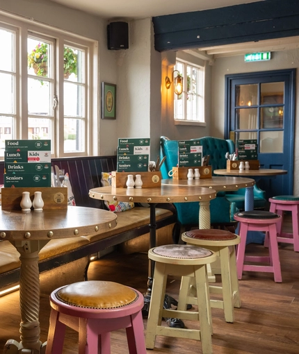 An interior restaurant seating area at The Royal Oak; with wooden flooring, and a long, padded bench seat against the window wall.