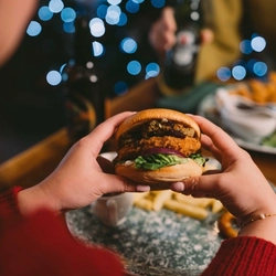 The hands of a person holding cutlery above a plated meal on a festive decorated wooden table.