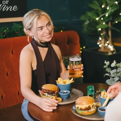 An image of 2 people enjoying burger dishes and a pint of Level Head while sat within the interior restaurant seating area.