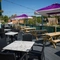 The exterior seating area on the deck of the Rudds Arms; with wooden picnic tables, shade umbrellas, and string lights overhead.