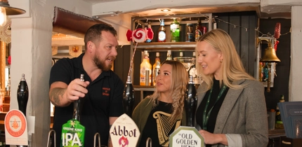 2 females talking to a male pouring a pint of IPA behind the bar