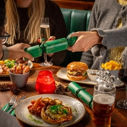 A table set for a festive meal.  Two people are pulling a Christmas cracker.  Their faces are not visible in the image.