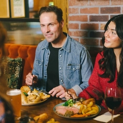 A lifestyle image focusing on 2 friends enjoying Sunday Roast dishes and drinks within the interior restaurant seating area at an Urban Core Venue.