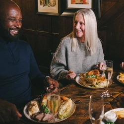 A lifestyle image focusing on 3 customers sat at a table enjoying Mothers Day main dishes and drinks within the interior restaurant seating area at a Heritage venue.