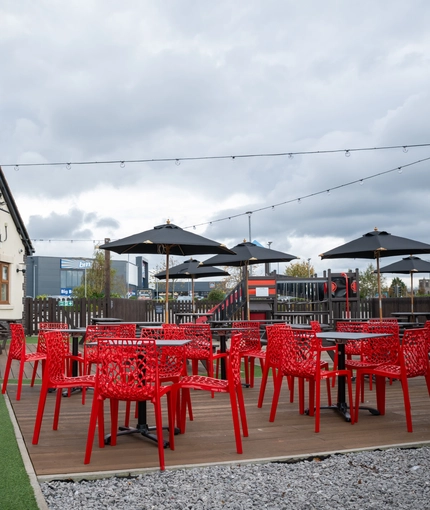 The exterior beer garden seating area at The Parsonage in Leigh, with string lights overhead and shade umbrellas at some of the tables.