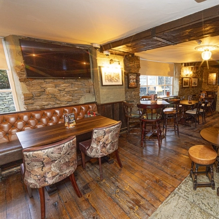The interior seating area with wooden tables, exposed brickwork walls, log burner fireplace, wall mounted TV screens and electronic pub game at The Flag Inn.
