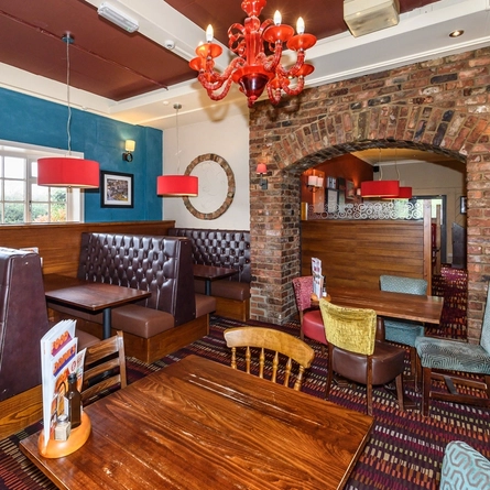 An interior restaurant seating area at the Spotted Cow in Coate; with upholstered booth seats, and brick wall archways.