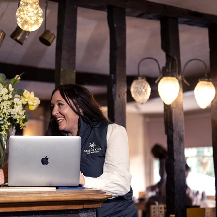 Two women sat at a table with a laptop, they are both laughing. 