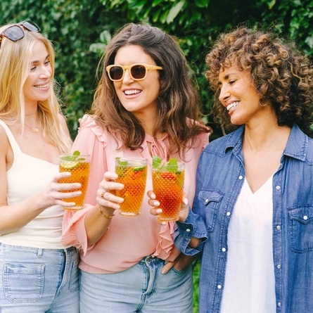 Three people standing in a beer garden, each holding a glass of Pimm's cocktail garnished with mint leaves and fruit.