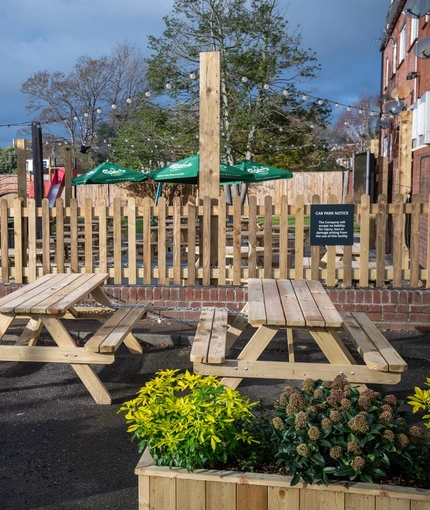 An exterior beer garden seating area at The Green Posts, with wooden picnic tables, and plants in wooden planter boxes.