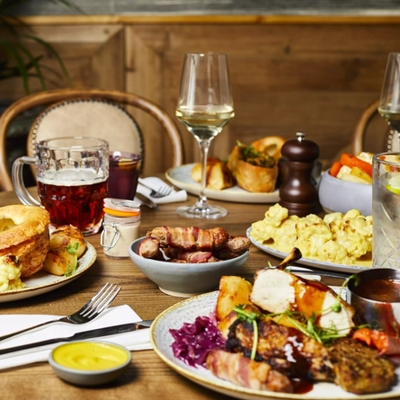 Plates of food and drinks sitting on a wooden table of a pub