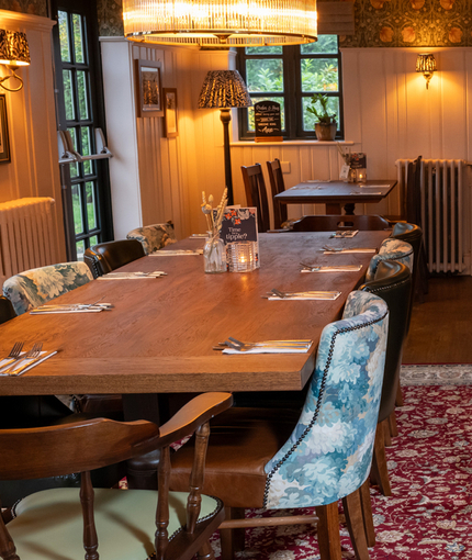 The interior restaurant seating area of Ye Olde Swan in Woughton-On-The-Green, with wooden beams on the ceiling and framed artwork on the walls.