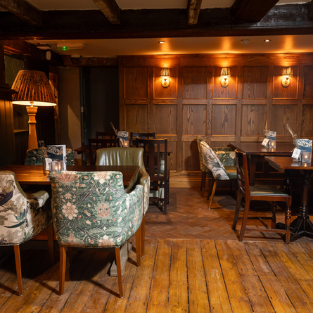 An interior restaurant seating area at The Rising Sun, with wooden flooring, wood panelled walls, upholstered chairs and a booth seat along one side of the room. 