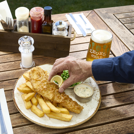A lifestyle image showing a person sat at a table within the exterior beer garden seating area enjoying a main dish and drinks at a Chef & Brewer venue.