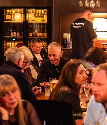 An image showing people stood at the interior bar and sat around tables within the seating area enjoying drinks at The Black Swan.