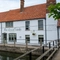 A view from across the river of the exterior facade of The Kings Arms in Sandford-On-Thames, and the wooden bridge leading across the water.