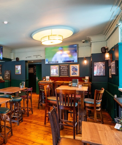 The bar and interior restaurant seating area at the Royal George; with wooden flooring, an upholstered booth seat, and TVs on the walls.