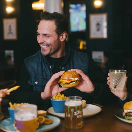 A lifestyle image of 3 friends sat within the interior restaurant seating area enjoying Burger dishes and various drinks available at Urban Core venues.