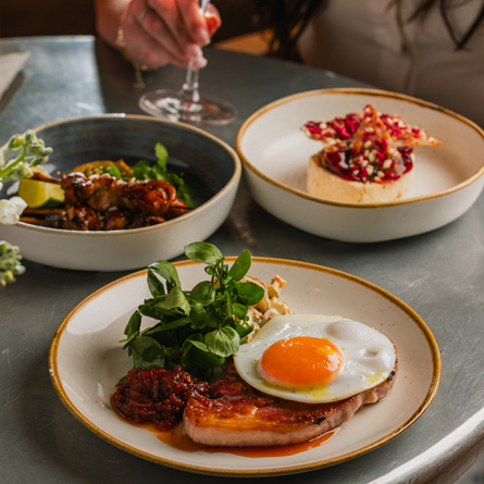 A lifestyle image showing a person sat at a table with 3 different dishes and a glass of wine at a Crafted venue.