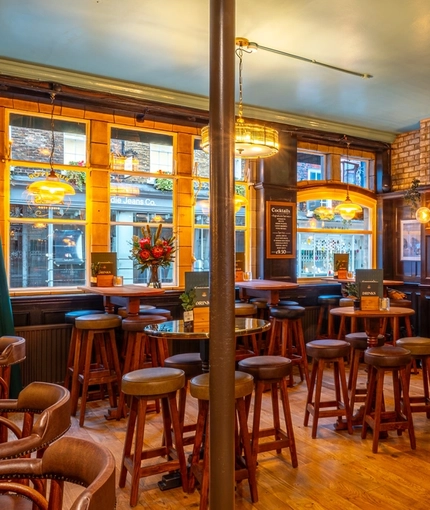 The wood panelled bar and interior restaurant seating area of The Two Brewers in Covent Garden, with a TV on the wall, and a fireplace.