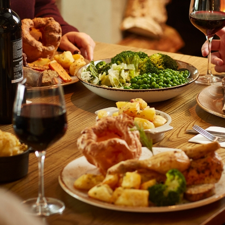 Plated Roast dinners on a table with people holding a glass of wine.