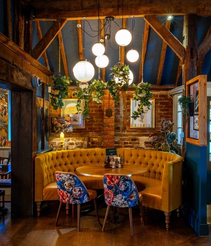 An interior circular booth seating area at The White Hart, with wooden beams, upholstered seats, and potted plants hanging above the table.