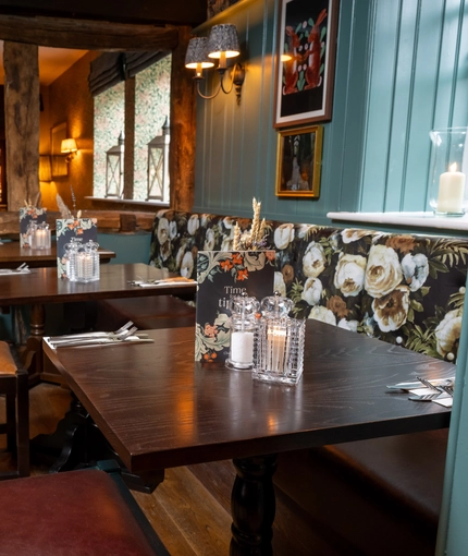An interior restaurant seating area at The Malthouse Farm, with an upholstered booth seat, wooden beams, and framed artwork on the wall.