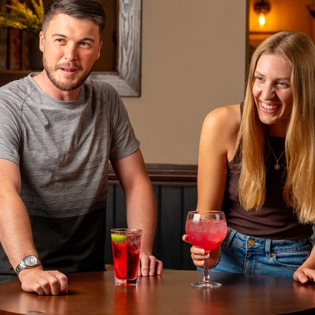 A man and a woman seated at an indoor table enjoying cocktails.
