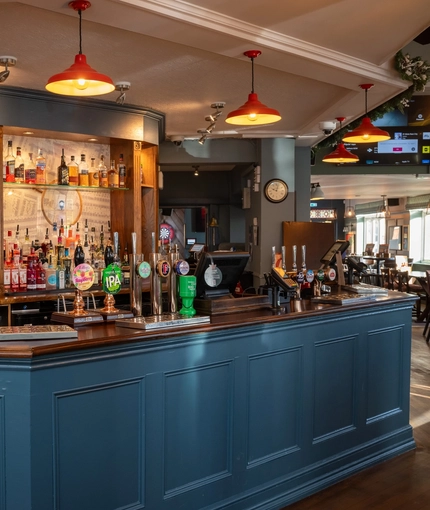 The bar inside the Green Posts in Portsmouth, with bottles of alcohol on glass shelves behind the counter.