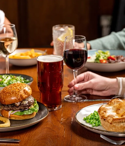A hand holding a glass of wine on a table with two plates of food in front of it.