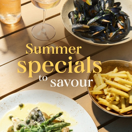 A banner showing 3 different dishes and 2 drinks sat on a table within an exterior beer garden seating area to advertise Summer Specials To Savour at Chef & Brewer venues.