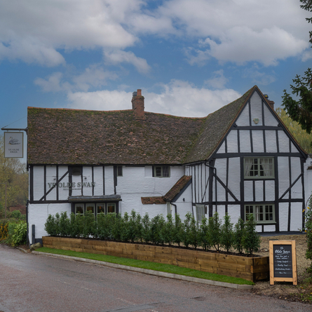 A view from across the road of the exterior facade and signage of Ye Olde Swan in Woughton-On-The-Green.