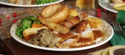 An advertising image of 3 plated Xmas Day Main dishes with a selection of drinks sat on a table within the interior restaurant seating available at Proper Locals venues.