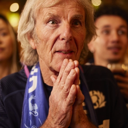An image of a man wearing a sport team scarf, watching a sporting event.