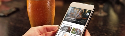 A phone with the Greene King app on it, being held by a person's hands.