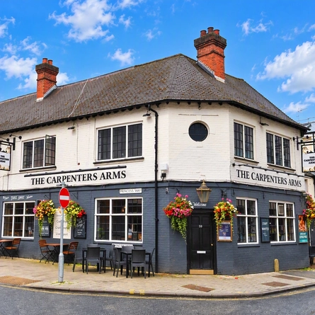 The exterior facade of the venue with venue signage, outdoor seating and hanging baskets at The Carpenters Arms.