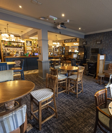 Interior dining area of a pub with a bar, a TV and gambling machines.