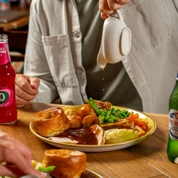 An image of gravy being poured over a Sunday Roast with various drinks within the interior restaurant and seating area at a Hungry Horse venue.