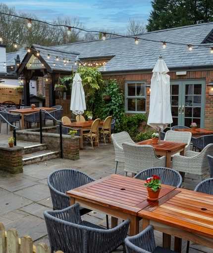 The exterior beer garden seating area at The Fox & Hounds in Bursledon, with wooden tables, wicker chairs, shade umbrellas, and string lights.