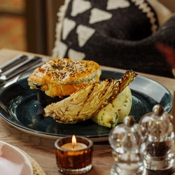 An advertising image of a Pie Choice dish and a pint of beer within the interior restaurant and seating area at The Foundry Bell.