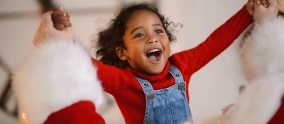 A child holding hands with someone dressed as Santa while smiling.